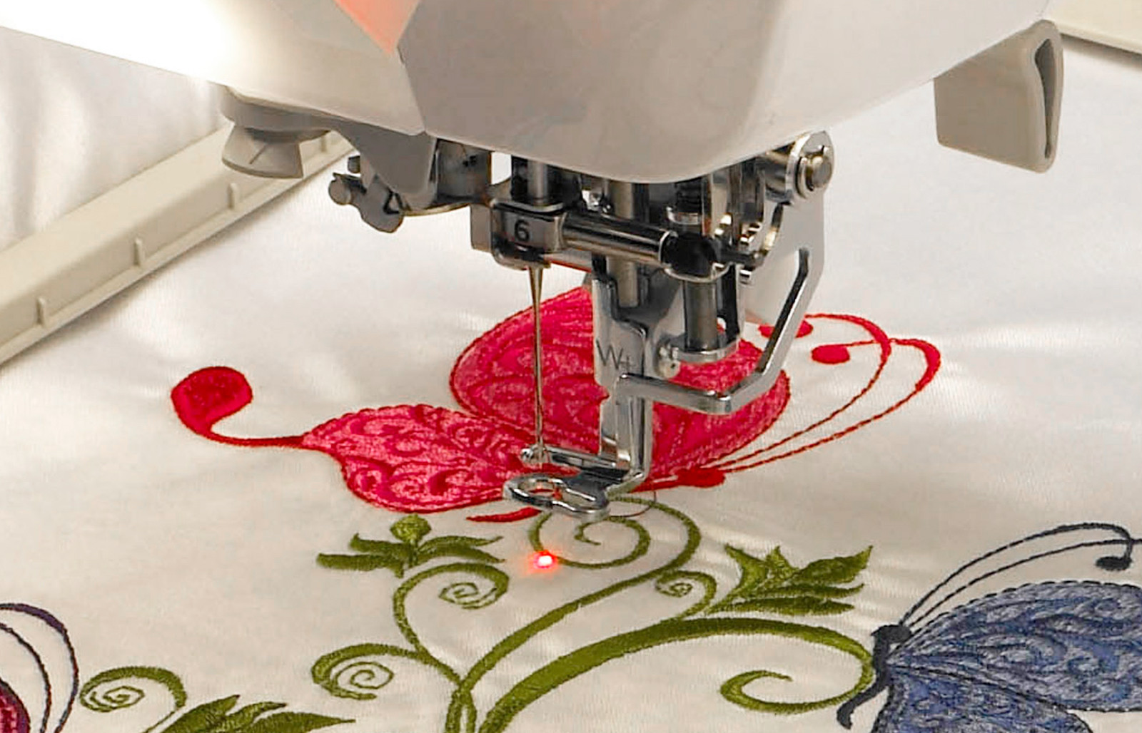 A close up photo of an embroidery machine with needle beam in action over flower and butterfly design